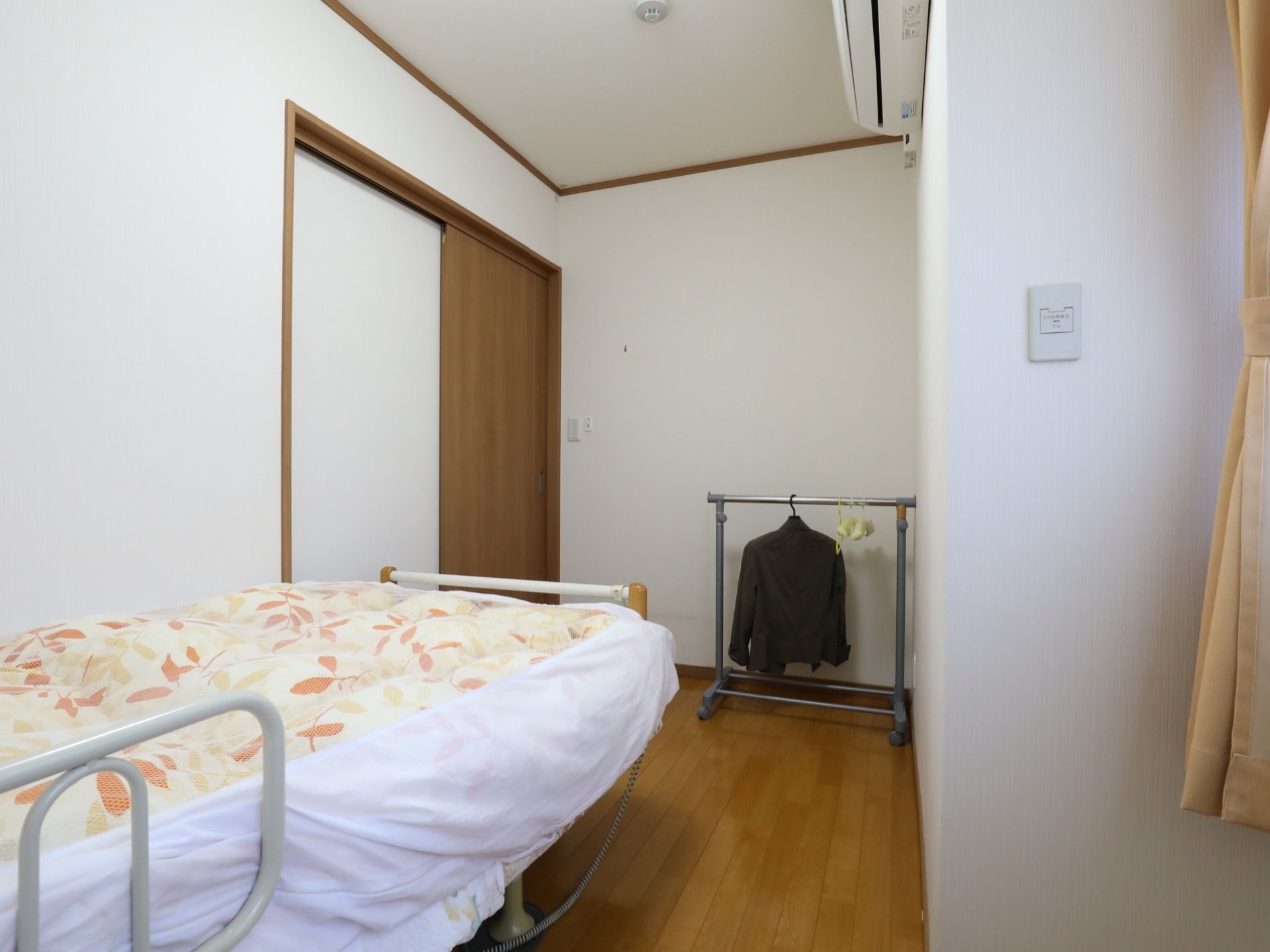 ベッドには立ち上がり補助を兼ねた落下防止柵が取りつけられている。エアコンが設置されており、一年を通して快適な室温で過ごすことができる。
