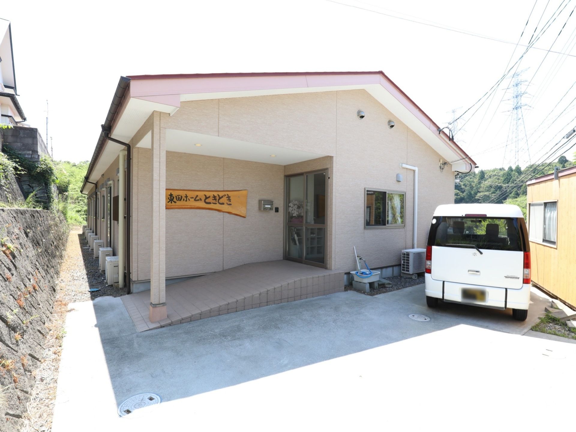 こぢんまりとした平屋建ての建物がある。玄関には緩やかなスロープが設置されている。壁には木の素材をいかした看板が掛けられている。