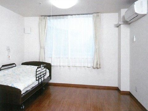大きな窓と手すり付きのベッド、エアコンが配置してある個室