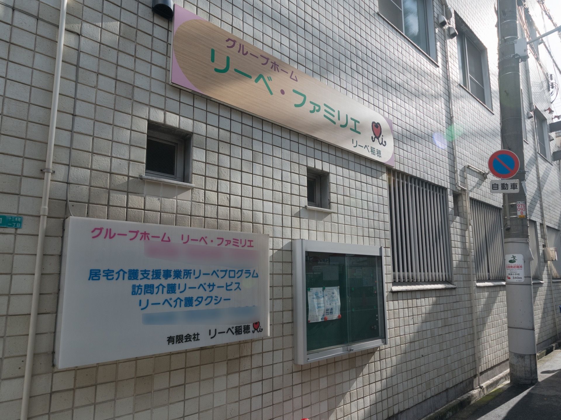 施設の外壁には施設の事業案内が書かれた看板が貼り付けられている。１階には窓があり、防犯対策として面格子がある。