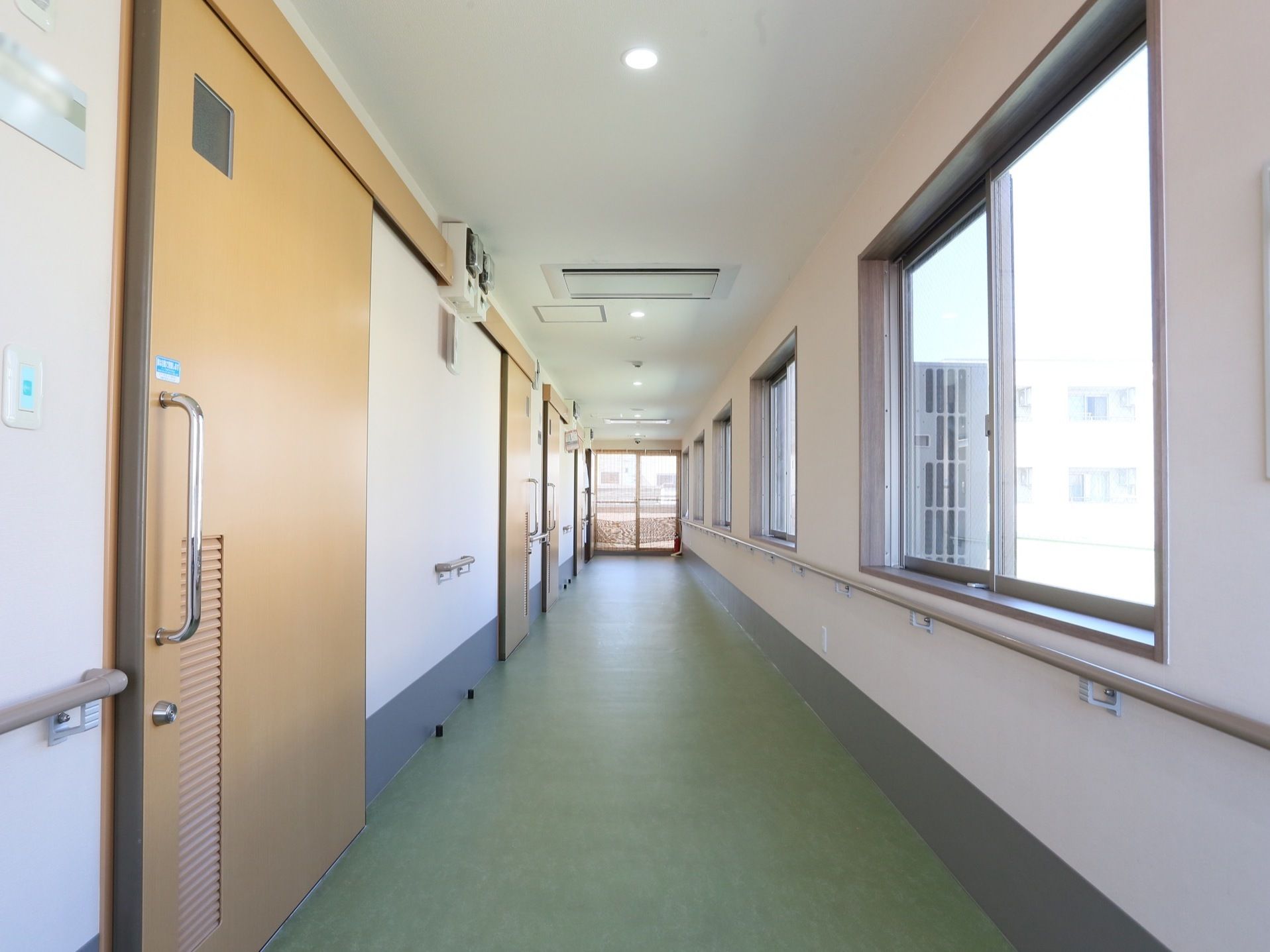 各居室につながっている廊下。窓の外にはビルが見えている。各ドアのストッパーは黒いゴム製のものが取りつけてある。
