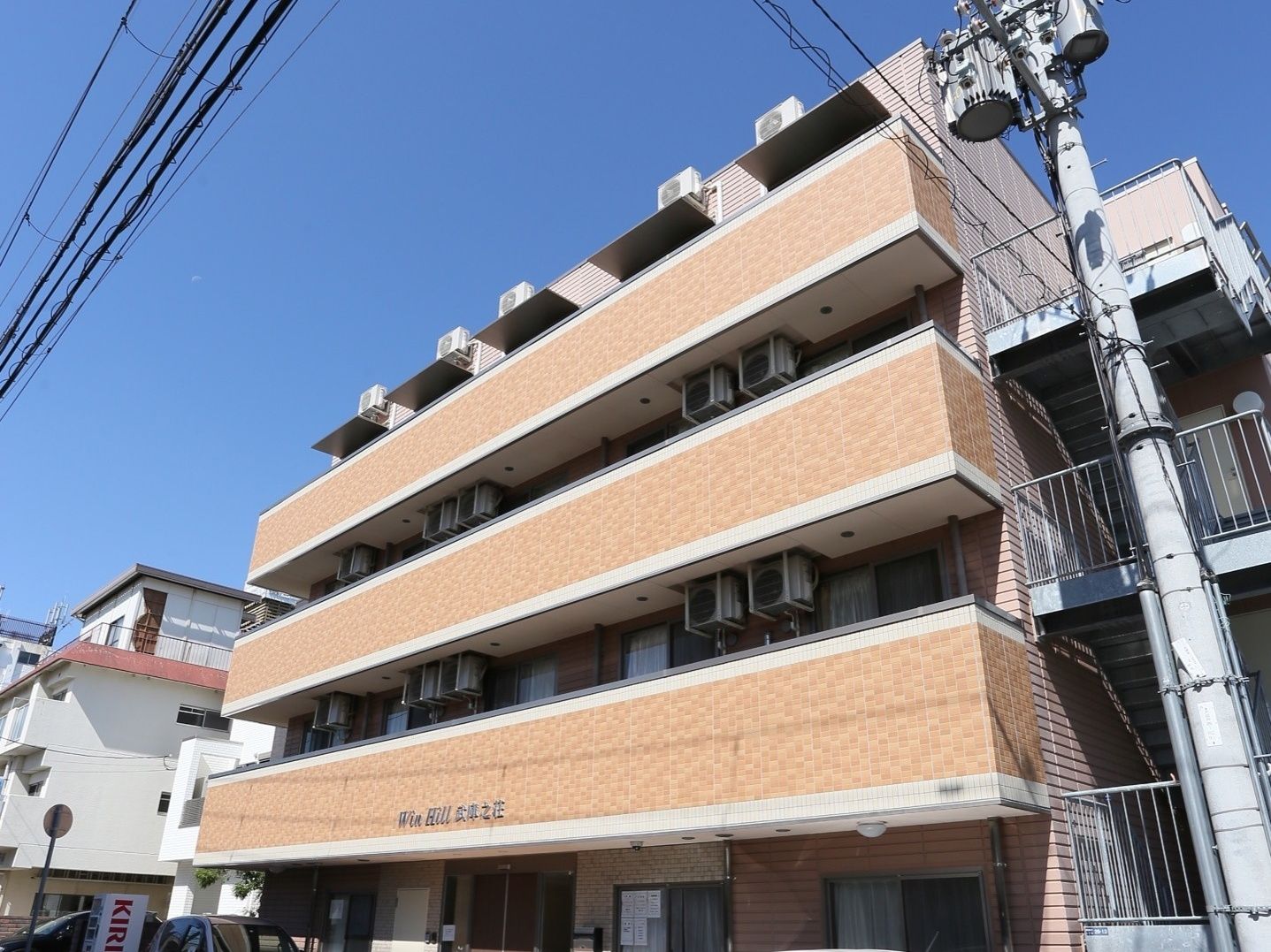 施設建物の外観。正面玄関はほぼ中央に配置されている。各部屋の前にはエアコン用の室外機が設置されている。