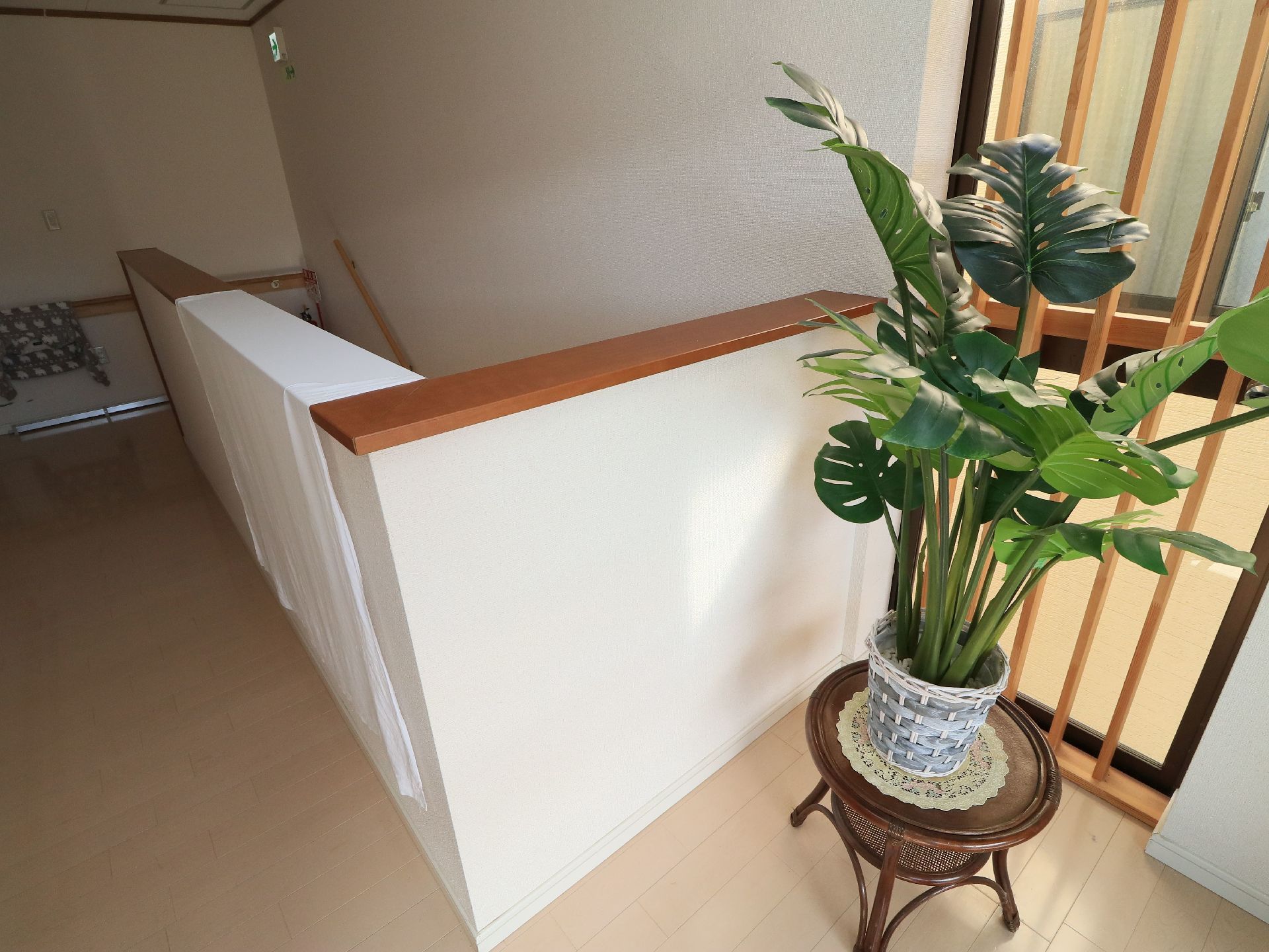 階段ホールには、観葉植物が置かれた丸い台がある。右に木製格子が設置された窓が設けられており、左奥の壁には手すりが設置されている。