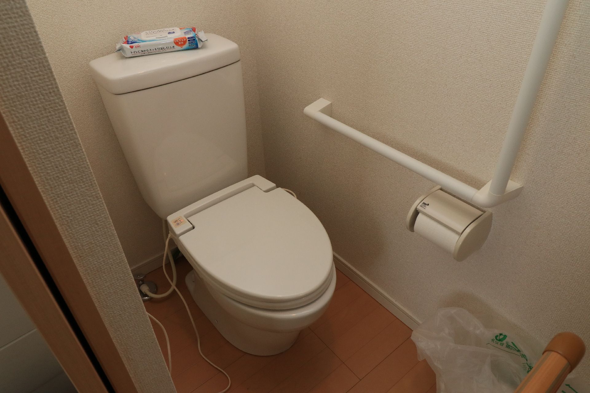 壁に手すりがあり、汚れたらすぐにふけるシートの置いてあるトイレ