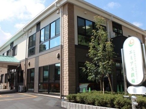 駐車場の入り口には大きな看板と木のある、施設の外観