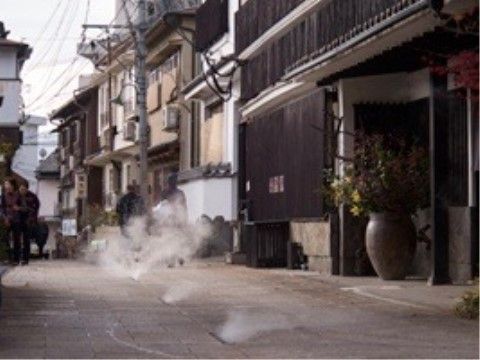 温泉宿が並ぶ街並みであり、古くからあるような趣のある建物が建っている。石畳の道路の間から湯けむりが漏れている。