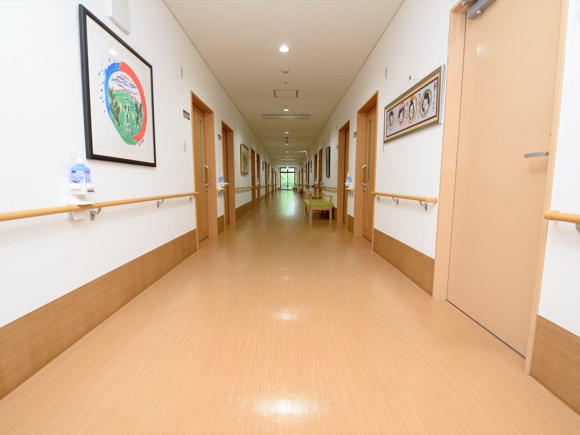 居室が立ち並ぶ長い廊下である。両サイドには手すりが設置されており、通路途中には椅子や消毒液が用意されている。