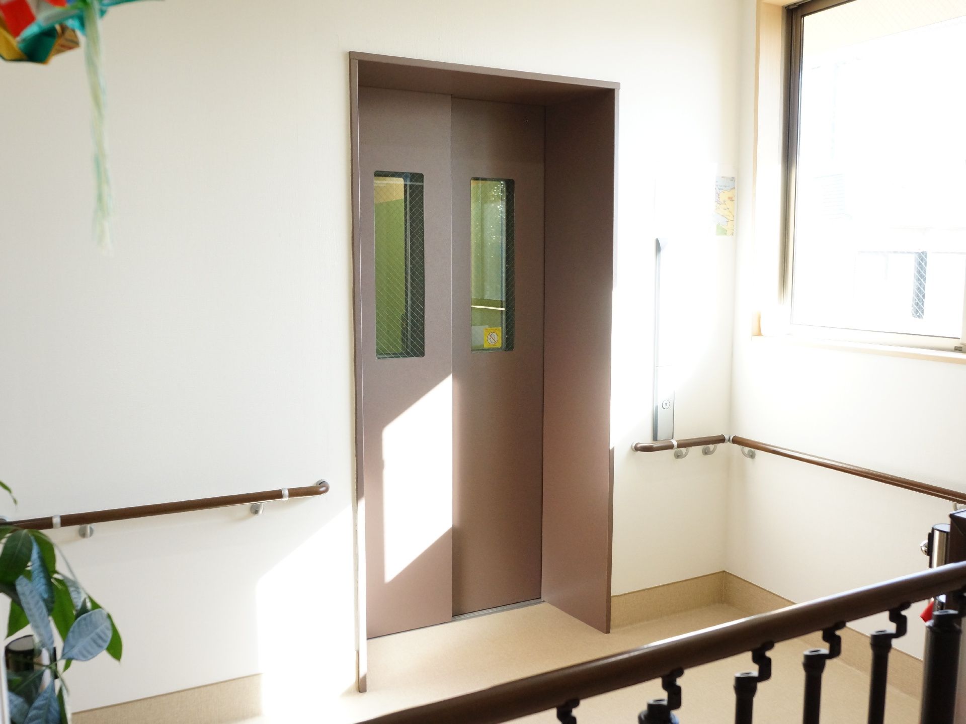 エレベーター出入り口は、陽が十分に差し込む窓があり、とても明るい空間になっている。また、壁に沿って手すりが設置されている。