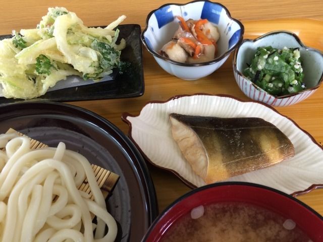 食事の一例です。ご飯、味噌汁、小鉢2種、お茶、そしてメインの煮魚がトレーにのっている。箸置きに箸がおいてある。