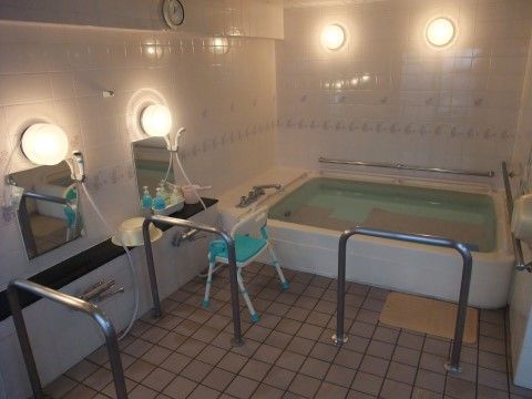 洗い場の前にシャワーチェアーが1台置かれている。転倒防止のために浴槽やシャワー周りに手すりを設けている。床は滑りにくいタイル張りである。