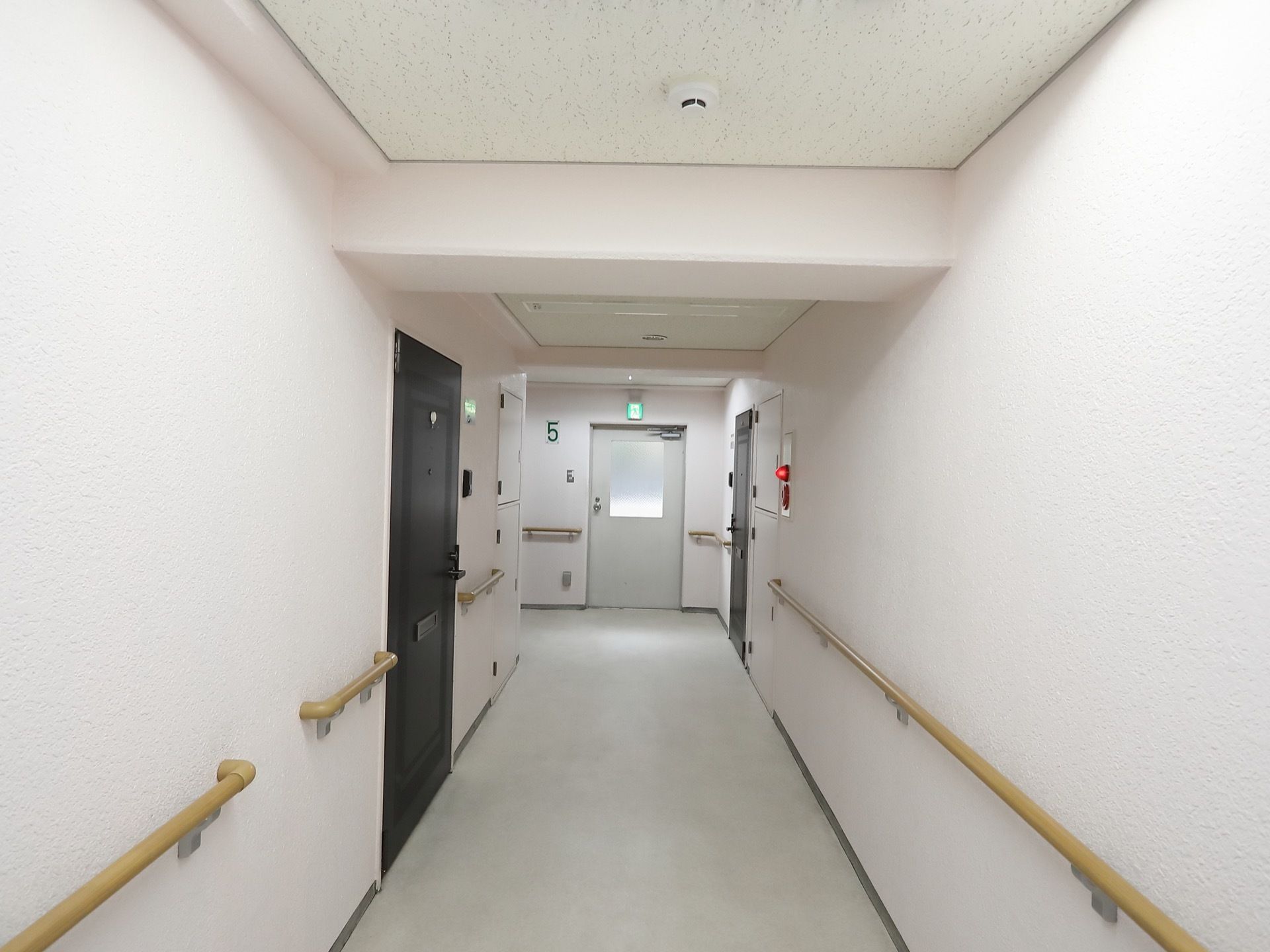 廊下の両側の壁に手すりが設置されている。つきあたりに見える扉は非常扉になっている。その横に、緑色の数字で階数が表示されている。