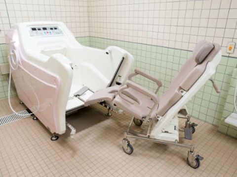 壁の上半分は白で下はグリーン、床はベージュのタイルの浴室。座ったままで入浴できる、介護入浴装置が置かれている。