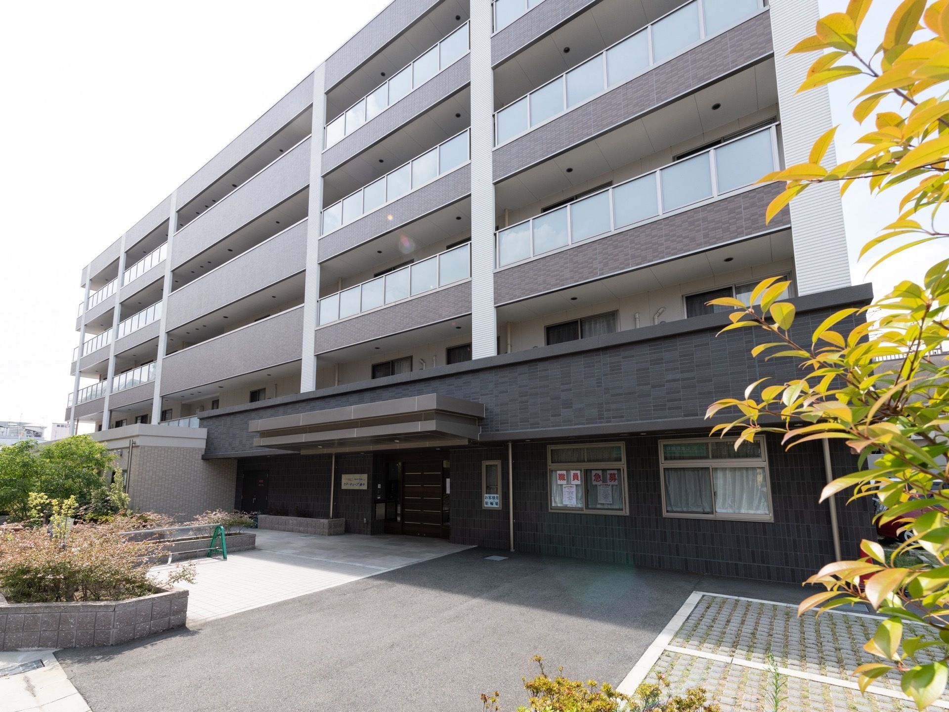 施設は黒や茶色を基調とした高層の建物で、各階にはベランダが設けられている。入口の前方をはじめとした周囲には、複数の草木が植えられている。