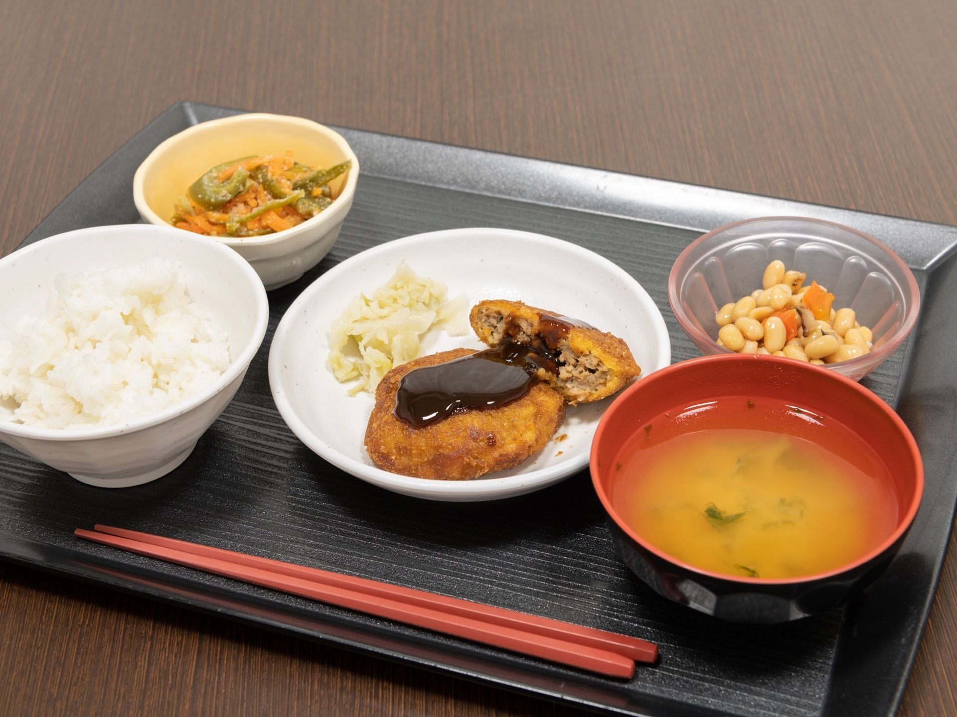 黒色のお盆の上に、ご飯とお吸い物、複数のおかずが丁寧に盛りつけられている。彩りも鮮やかで、多すぎず少なすぎない、適切な量が提供されている。