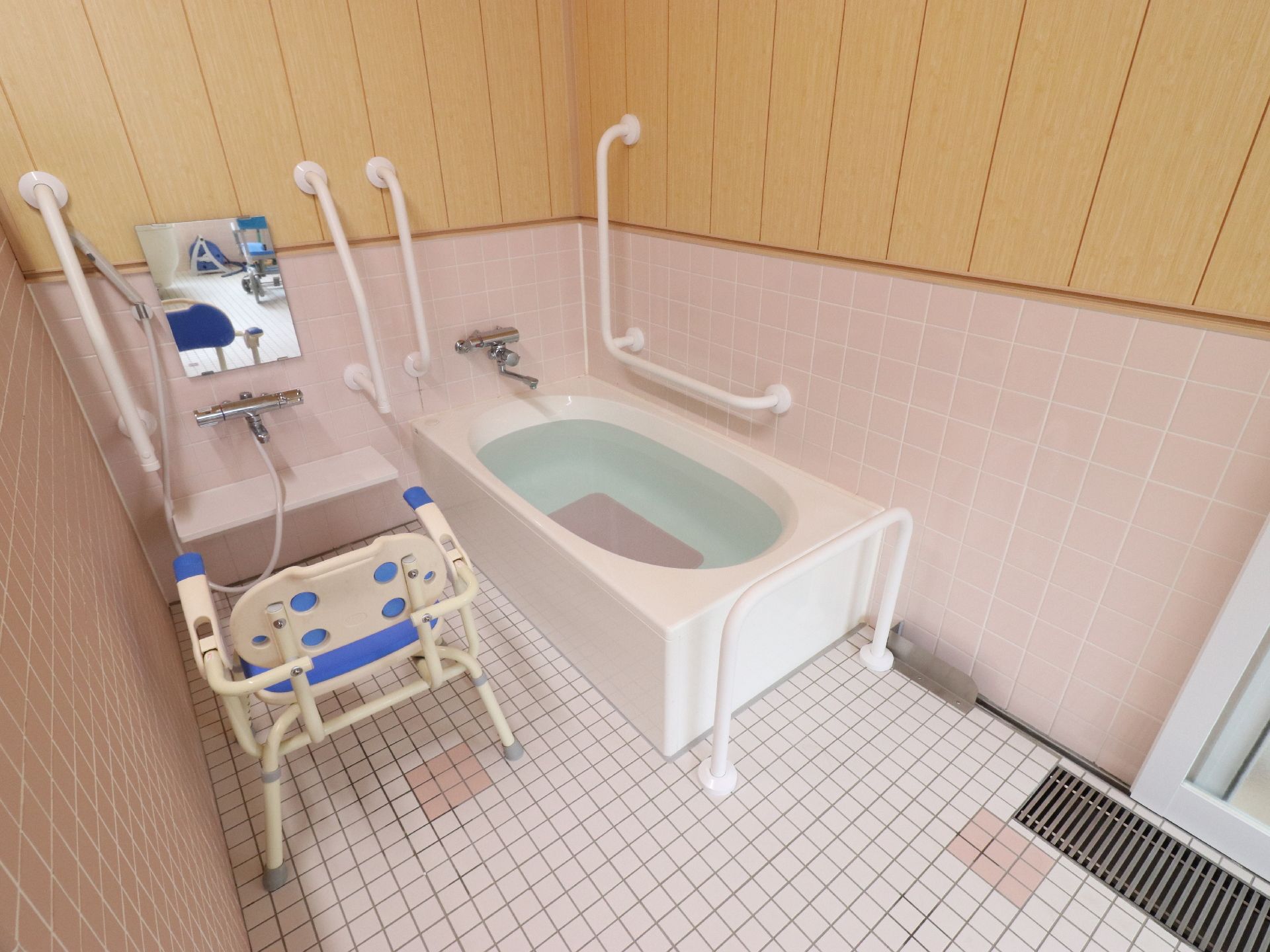 ピンクの腰板が明るい雰囲気の浴室には周りに手すりが設置されている浴槽と広々とした洗い場が設けられている。