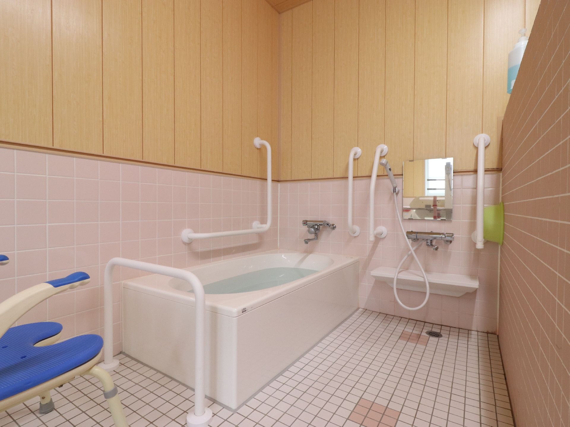 ピンクのタイル張りの腰板とベージュの壁が明るい雰囲気の広々とした浴室にはゆったりとした浴槽が置かれている。
