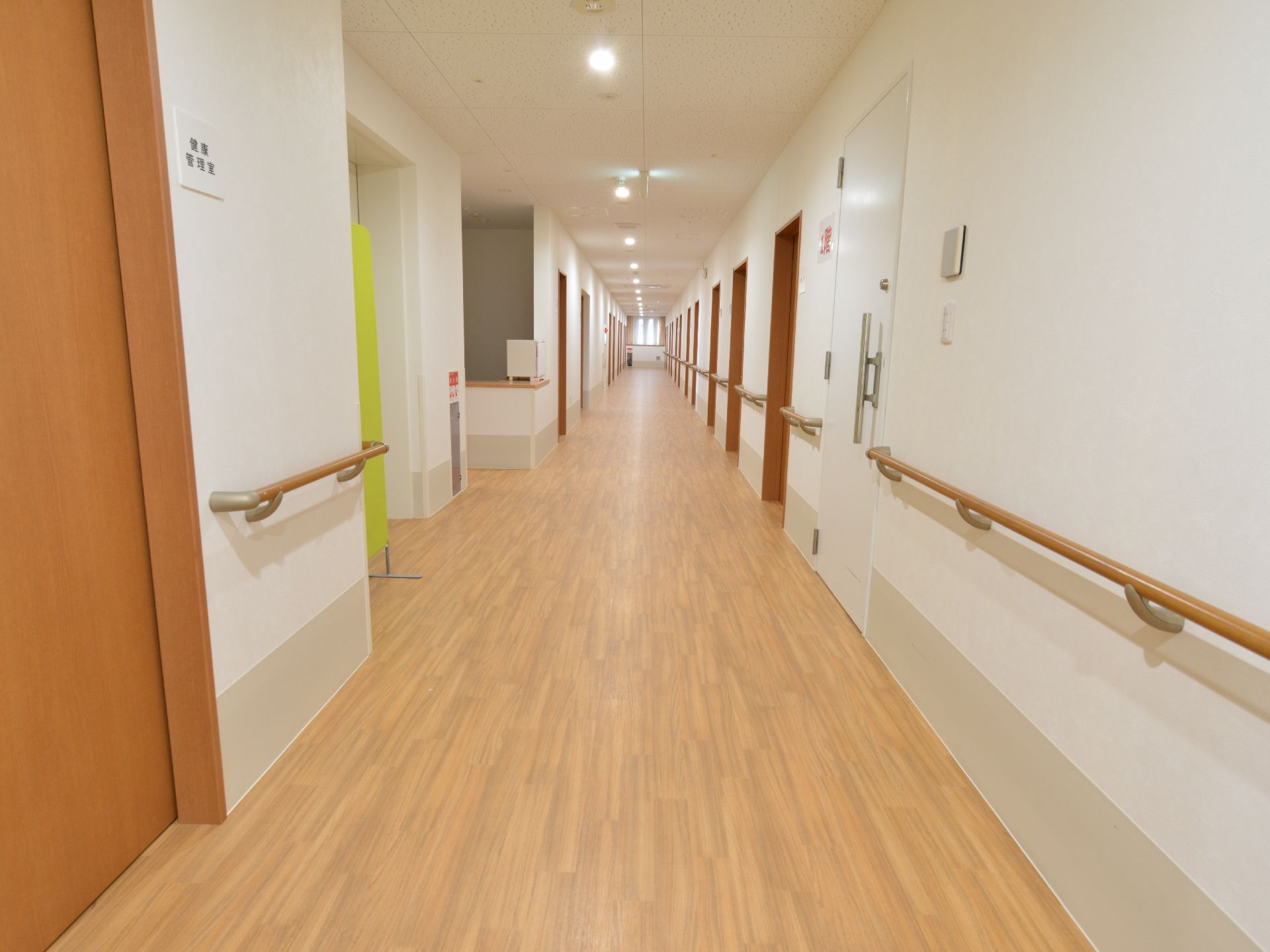 廊下の壁は白で床は茶色のフローリング。壁には全て手すりが設置されている。通路は幅広で車椅子が二台並べる広さがある。