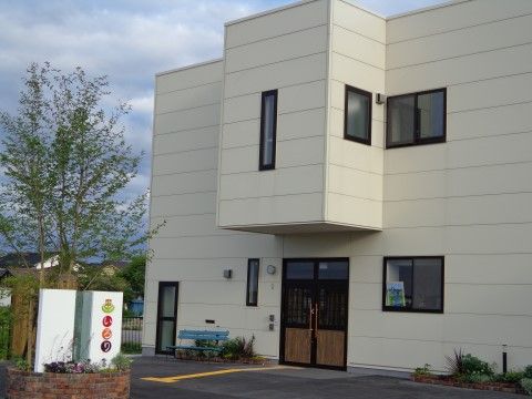 外壁がアイボリーで、2階建ての施設の外観。少し飛び出た2階の構造が、エントランス部分のひさしになっている。