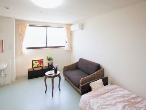 白い壁の明るい居室には、入居者様の人柄までうかがえそうないろいろな私物がある。ゆったり座れるソファーや、フォトスタンドなどが置かれている。