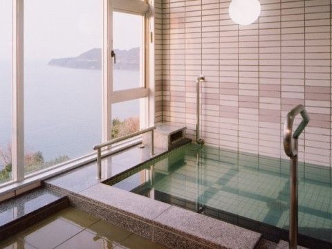 石造りの流し場にタイルの湯船。湯船には手すりが付いている。大きな窓からは眼下に海が広がっているという絶景である。