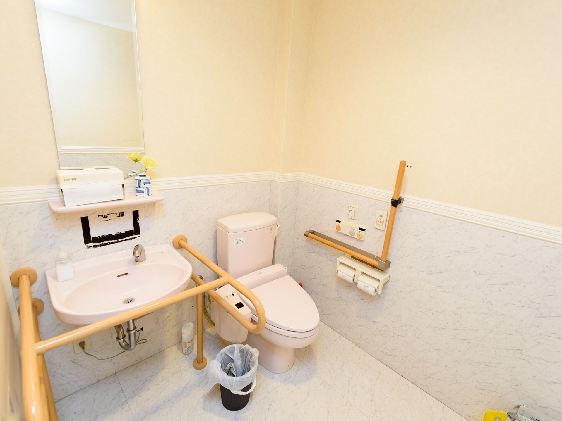 淡い色合いでまとめられた、明るくかわいらしい雰囲気のトイレである。便器の左側や洗面台の周囲に手すりが設置してある。