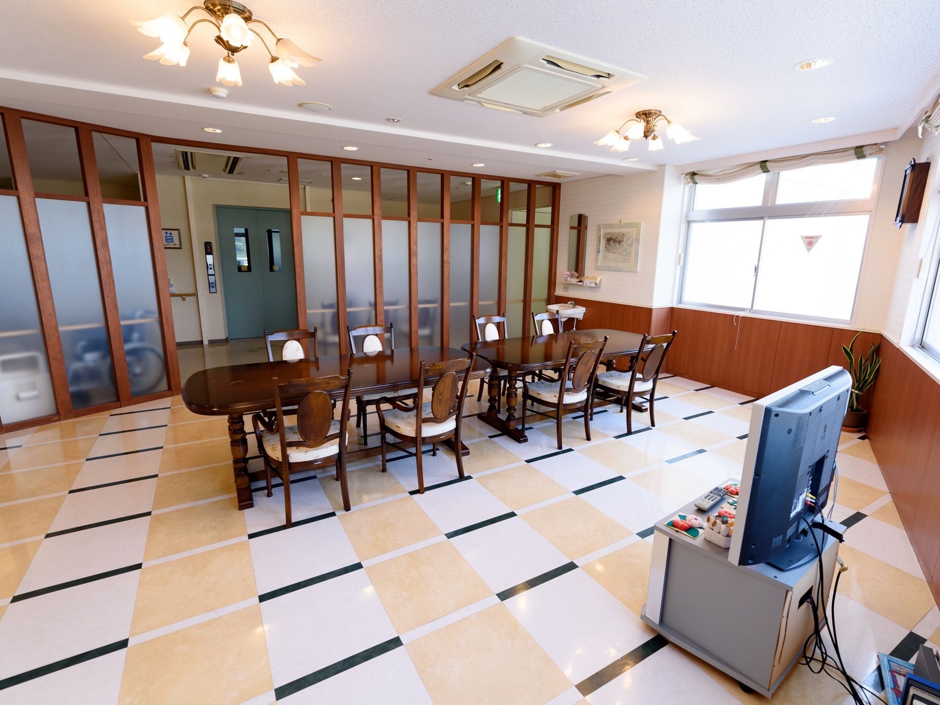 すりガラスに囲まれた凝った装飾の部屋に、ダークブラウンのテーブルと椅子が設置され、テレビが１台用意されている。