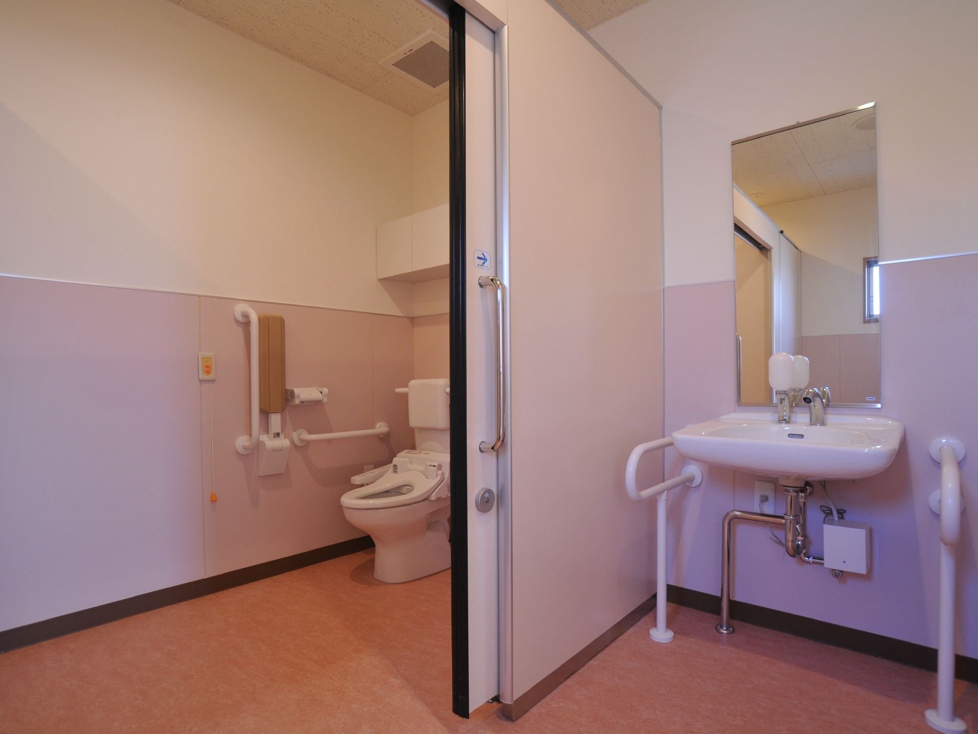 洋式トイレには、手すりが設置されている。緊急用ブザーが壁に設置してある。予備用トイレットロールが設置してある。隣接して手洗い場がある。