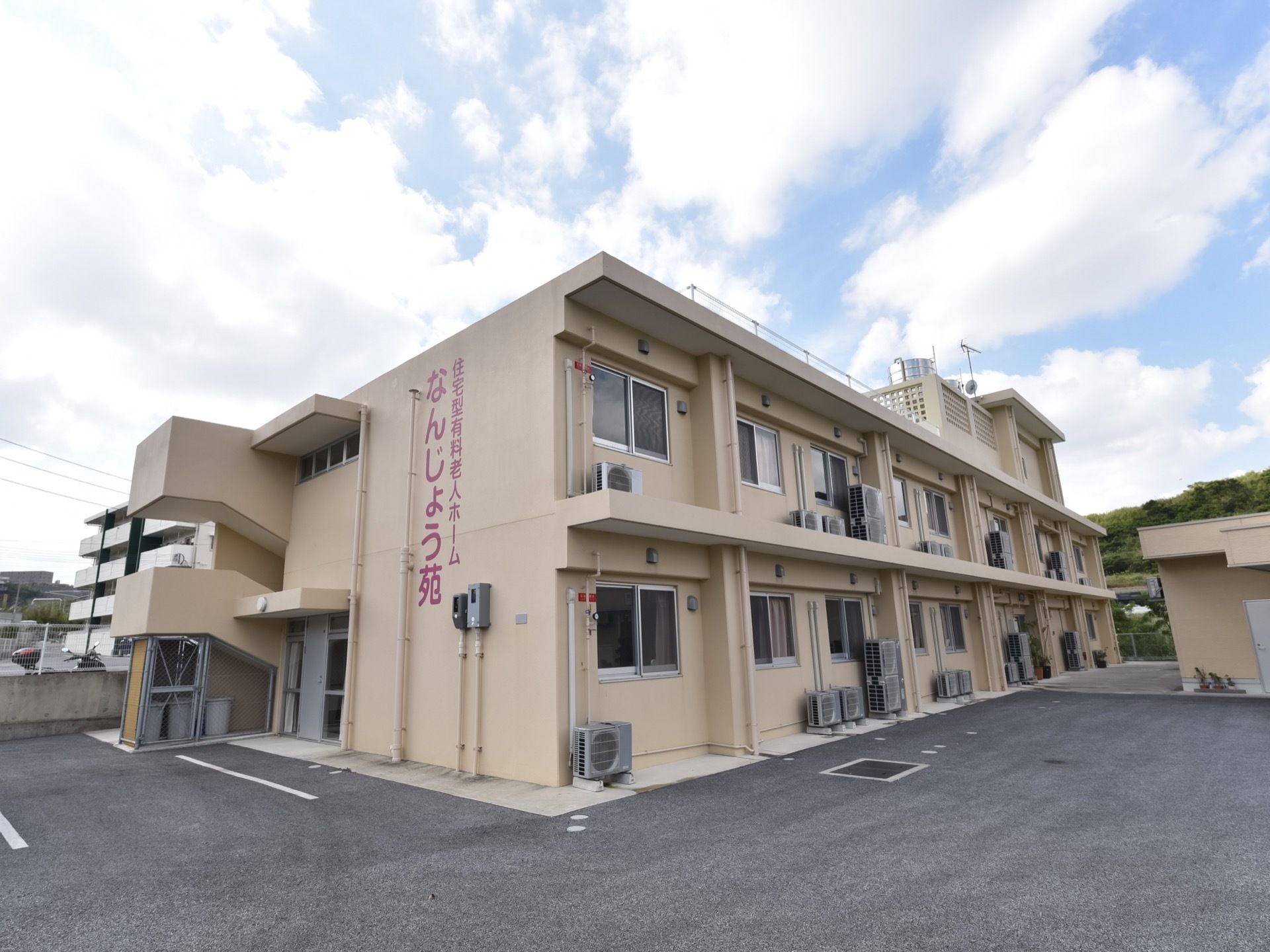 施設の建物は2階建てで、外壁はベージュ色をしている。外階段があり、屋上も見える。周囲はコンクリートが敷かれている。