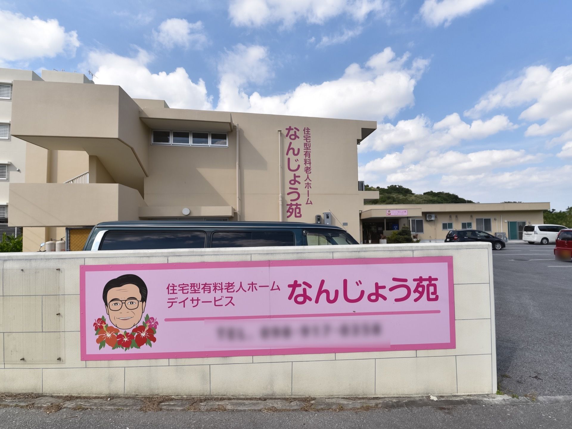 敷地入口の様子。ベージュ色に塗られたブロック塀があり、ピンク色のボードにイラスト入りで施設名が大きく表示されている。