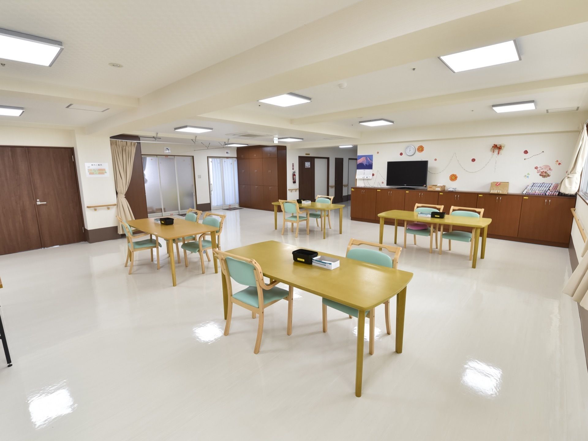 広々とした部屋の中にテーブルが4台あり、それぞれに揃いの椅子が置かれている。部屋の奥に、テレビが設置されている。
