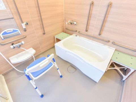 施設内で介護の必要の低い入所者が使用する一般的な浴室。木目調の壁とそこに取り付けられた手すりが特徴的。