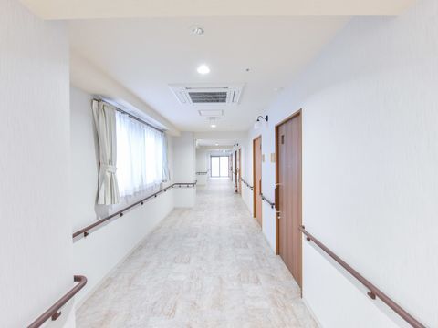 真っ白い廊下が続いている様子。廊下の片側にのみ個室が並ぶため、その反対側の手すりはドアで途切れている点がない。