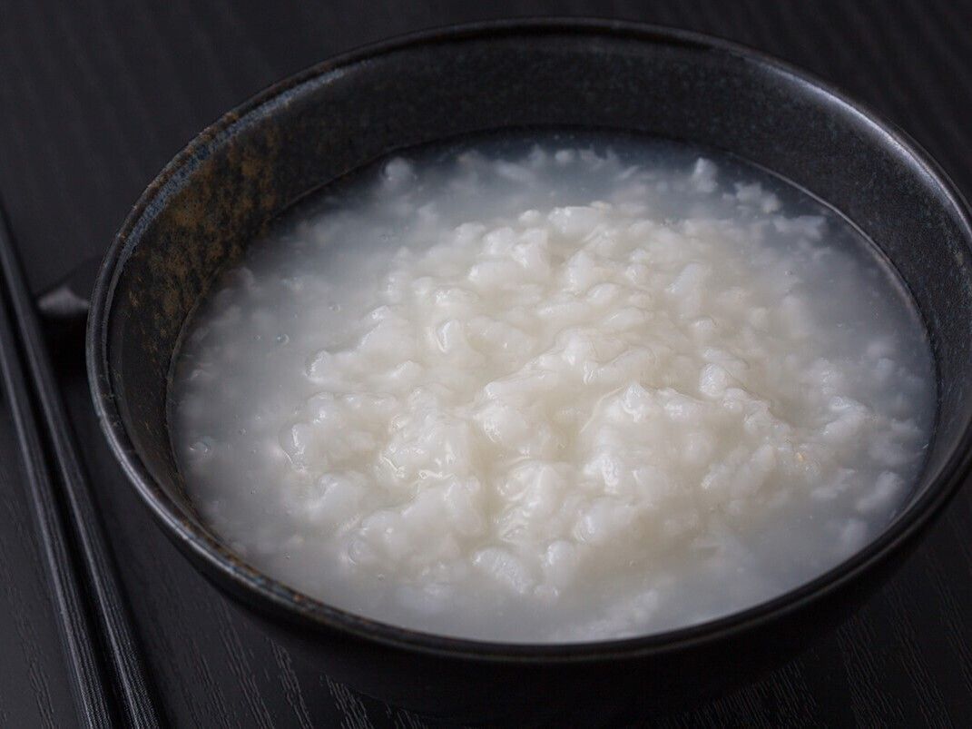 黒い茶碗によそわれた白米のおかゆと、箸置きに並べられたお箸