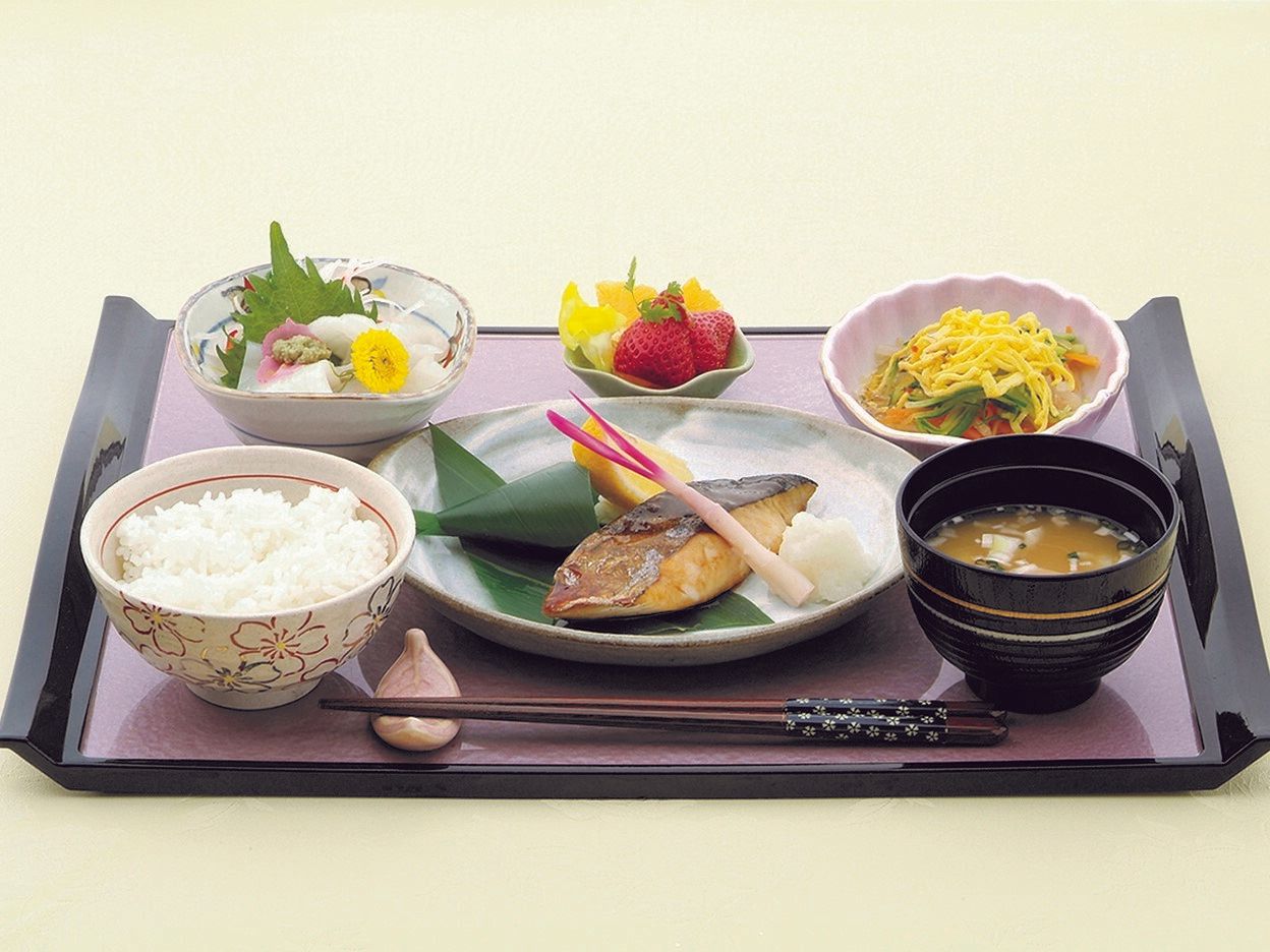 華やかなデザインのお盆に置かれた、焼き魚をメインにした和食膳