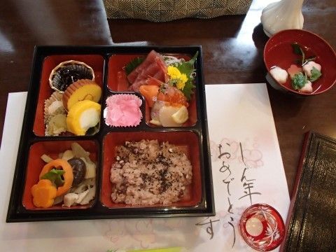 伊達巻、煮物など様々な料理が重箱に詰められ、お吸物が添えられた新年の料理