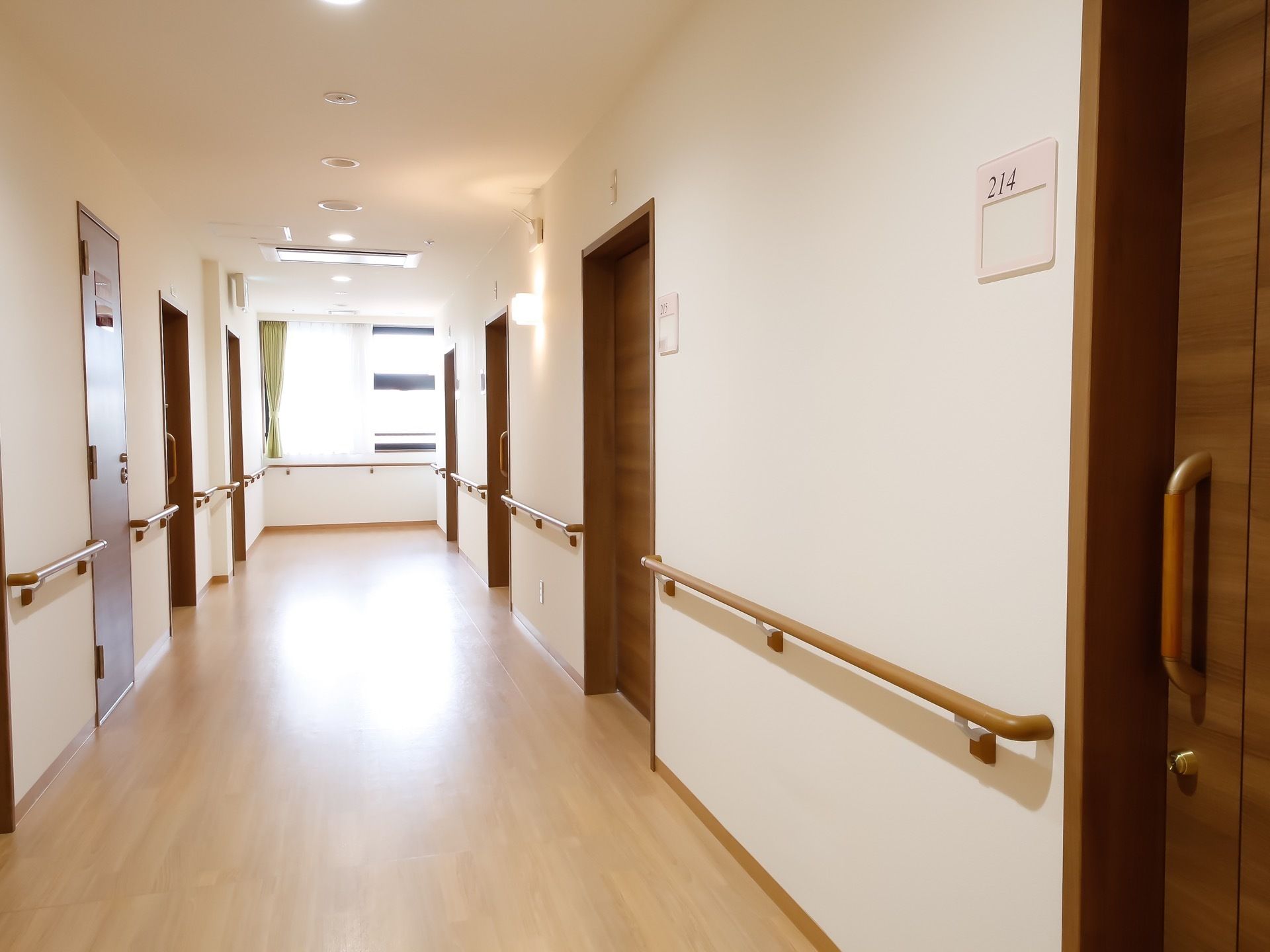 部屋の前の通路の壁には手すりが設置してある。突き当りの窓からは外の光が差し込み、通路を照らしている。