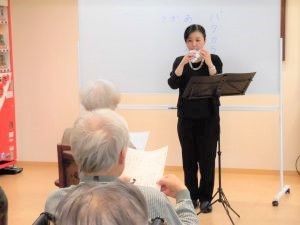 入居者たちの前で音楽療法士が増えのようなものを吹いている。