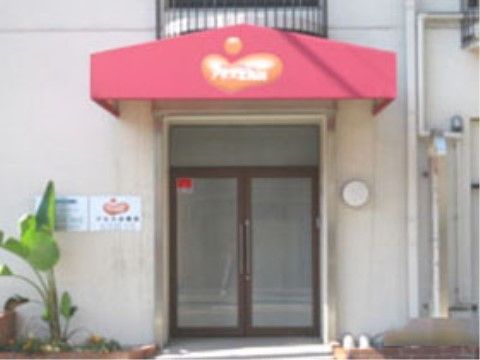 施設の入り口は喫茶店のようなかわいらしい赤いアーケード屋根が取りつけられている。扉横に施設名が表示されている。