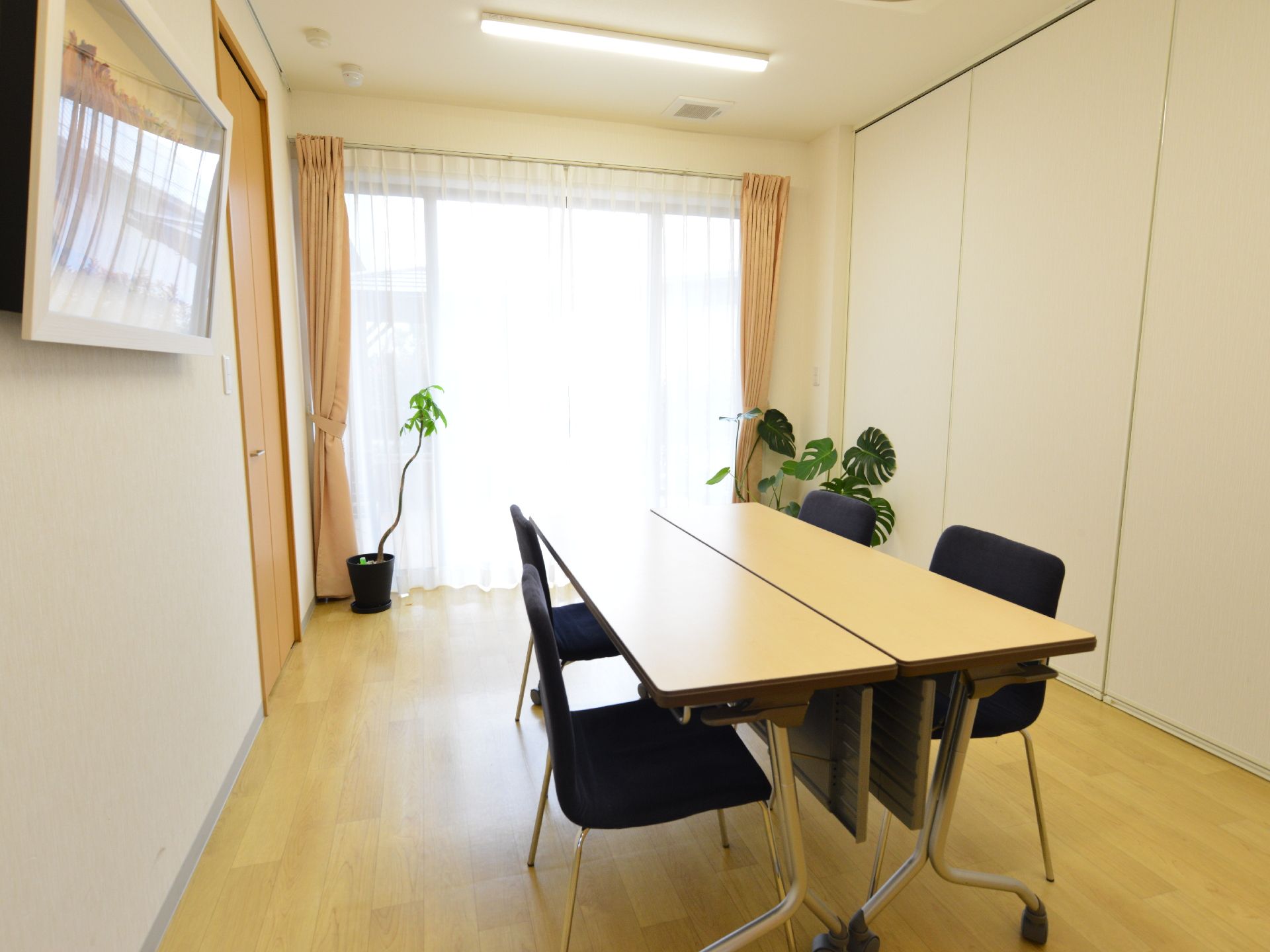 スタッフと入居者、その家族が話をする個室。大きい窓から日差しが差し込み明るい。観葉植物が置かれ、部屋の片側はパーテーション。