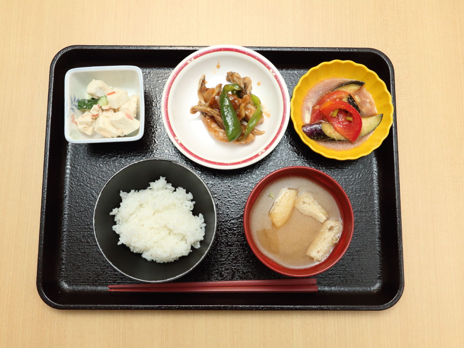 黒いトレーの上に食事が乗っている。ご飯やみそ汁、野菜や肉を使った栄養バランスの良いおかずが並んでいる。