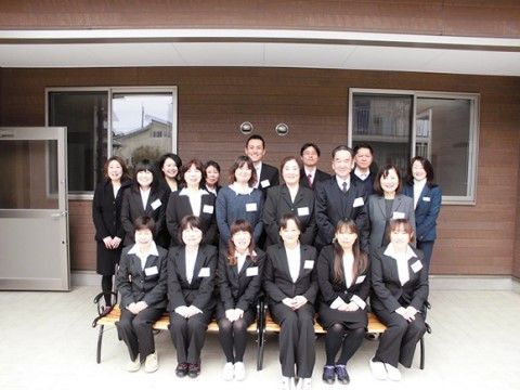 建物前に置かれたベンチに集合し、写真に納まるスーツ姿の人々