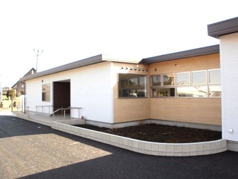 白い外壁の平屋の建物となっている。入口に続くスロープには手すりが設置されている。周囲に大きな建物はない。