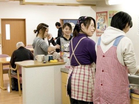エプロンを着用したスタッフがシンクで作業をしている。カウンターには入居者様のマグカップが置かれている。