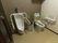 シックな色合いの壁紙のトイレに、洋式トイレと男性用トイレが設置されている。ナースコールや手すりが備わっている。