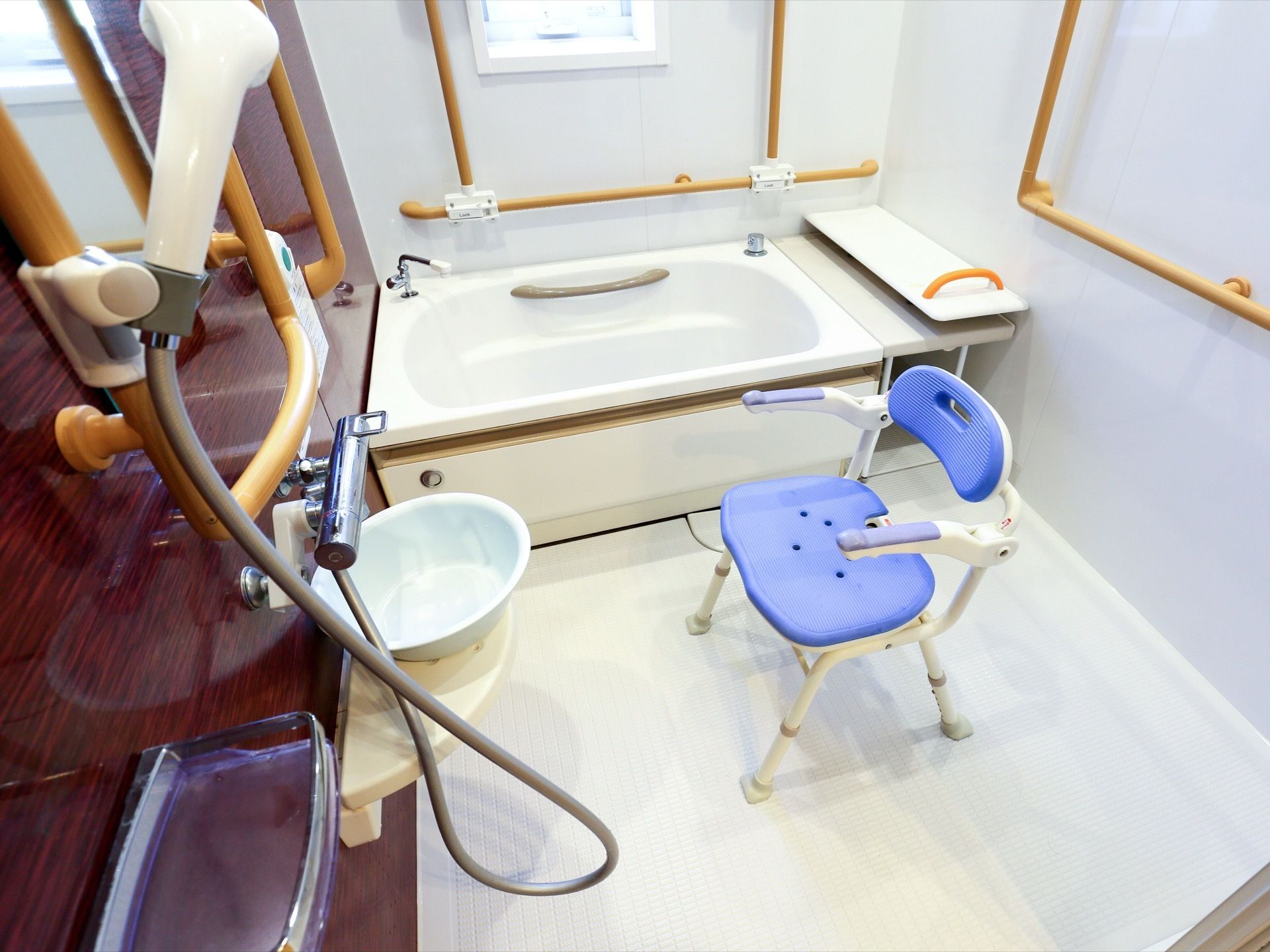 壁片面が茶色に施された、おしゃれな浴室である。随所に手すりがある。ブルーのシャワーチェアも置かれている。