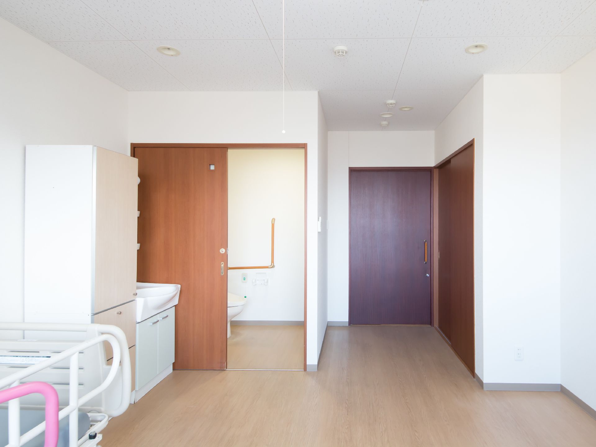 居室の一角にトイレがあり木目調の引き戸が設置されている。その横の壁際に洗面台と収納棚が置かれている。