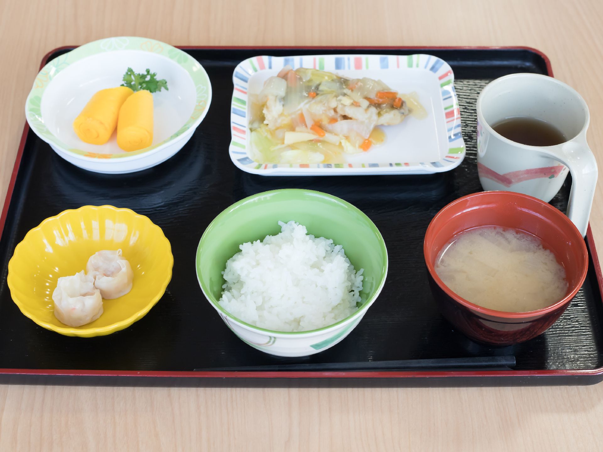 黒い四角形のトレーに食事が乗せられている。ご飯と味噌汁、お茶、おかず３品がきれいに盛りつけられている。