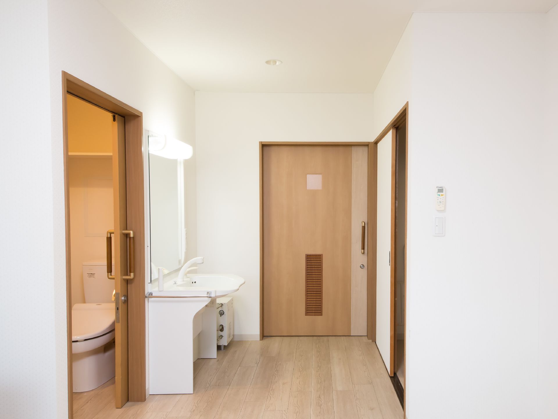 居室の入口扉は引き戸になっている。入口横に洗面台とトイレがある。洗面台の上に照明があり点灯している。