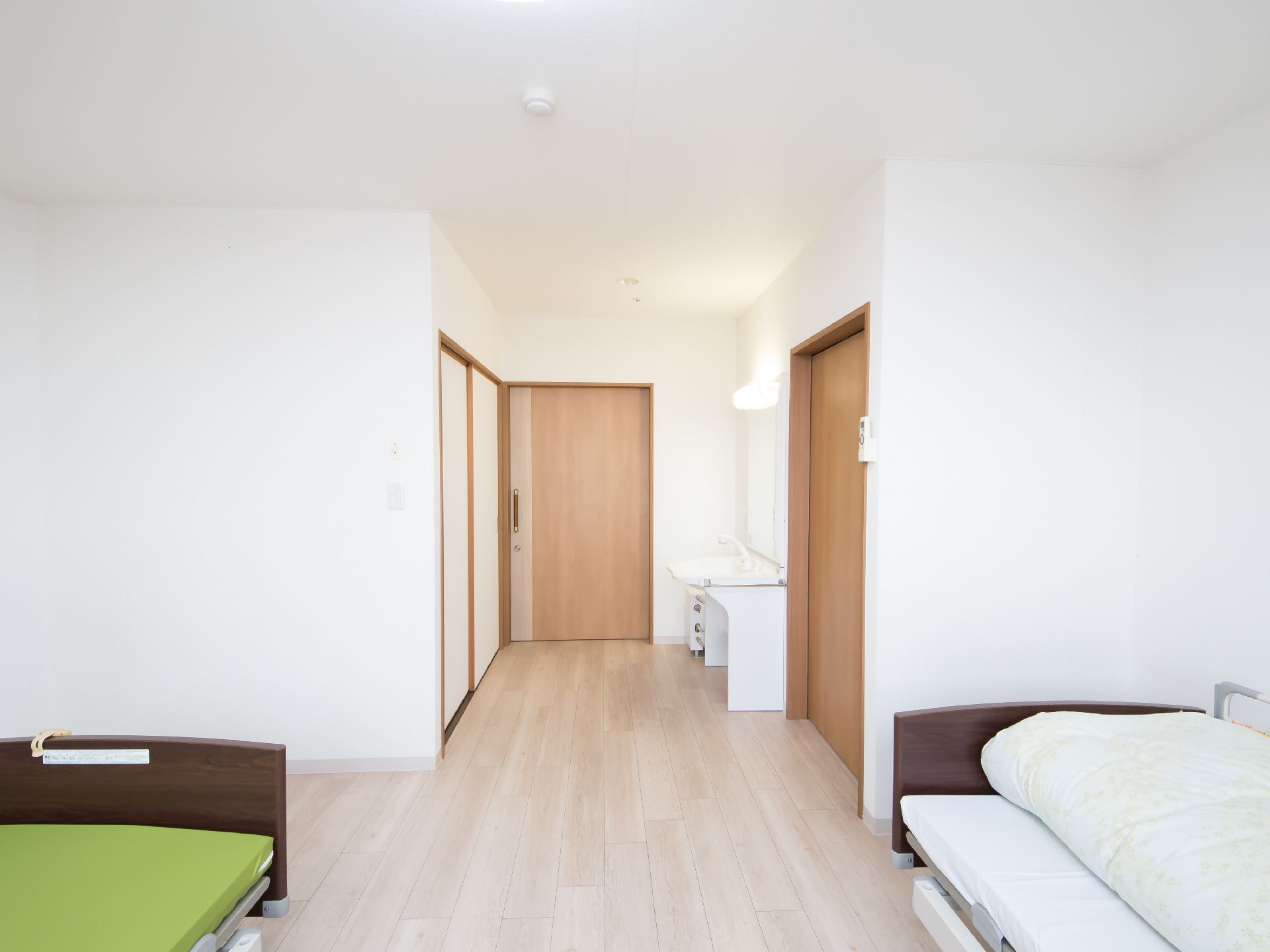 ２人用居室の一例である。入口を入るとトイレと洗面所がある。手前に居住スペースがあり、ベッドが２台置かれている。