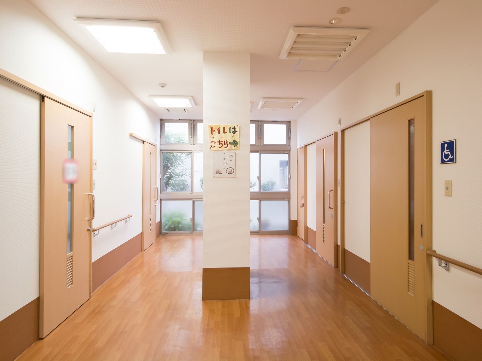 茶色い木目のフローリングの床の通路があり、突き当りに窓が設置されている。通路の途中に太い柱が立っている。